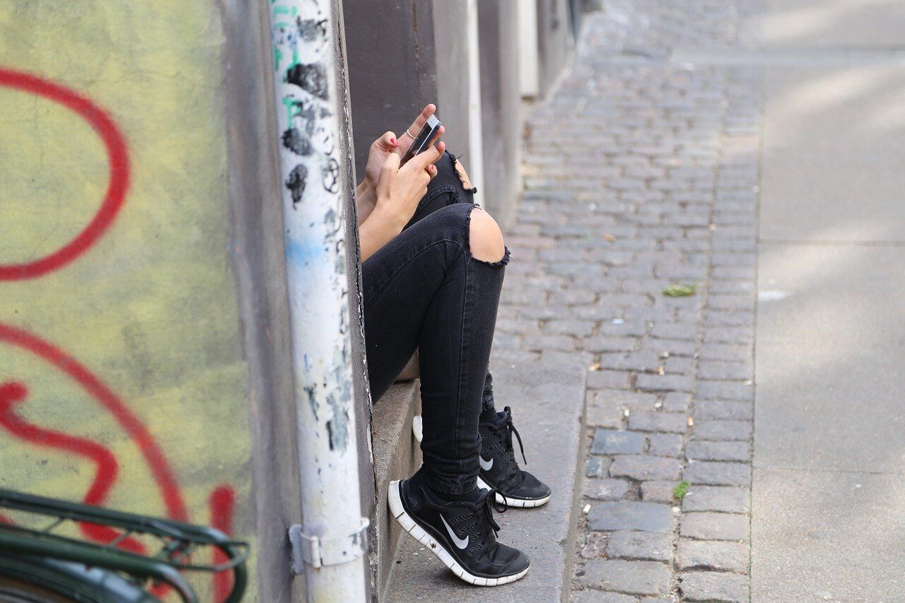 Imagen de una chica usando su teléfono mientras está escondida